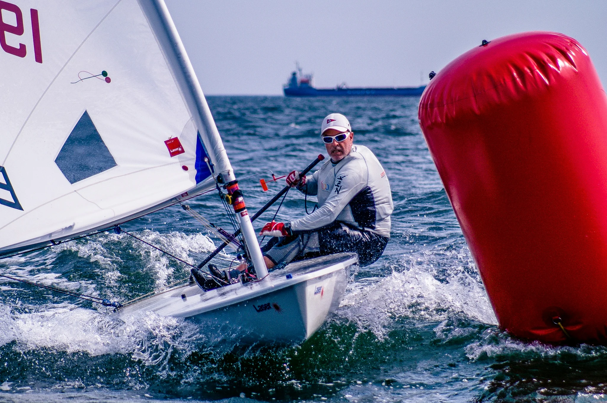 Sailor steering a dinghy around a red buoy at sea
