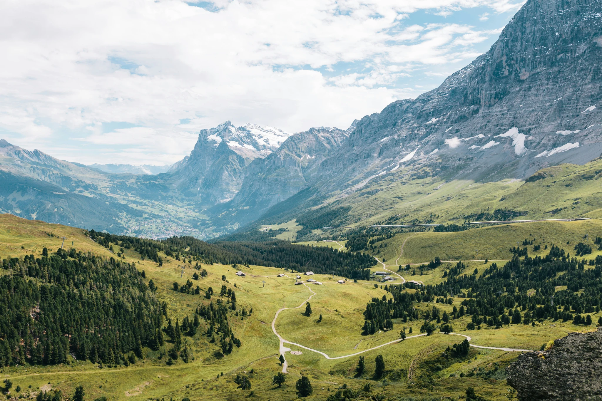 Green alpine meadows and forested slopes beneath steep mountain peaks